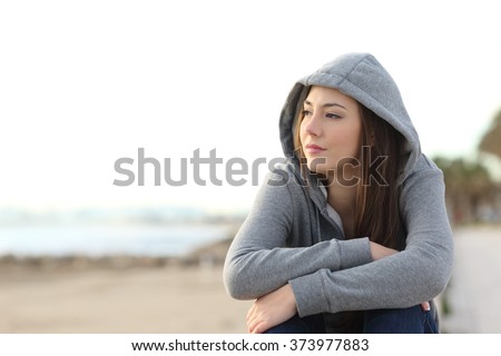 Portrait of a longing pensive teenager sitting on the beach looking away at the horizon in the morning