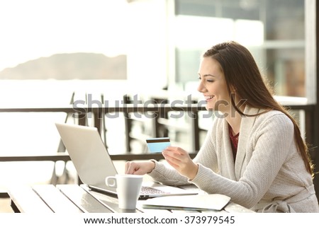 Portrait of a woman buying on line or booking hotel with a laptop and credit card on the beach in vacations. E commerce concept