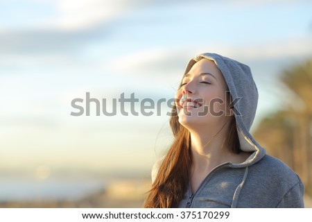 Portrait of a teenager girl wearing hood breathing deep fresh air on the beach at sunrise in a summer sunny day with a beautiful warm sky in the background