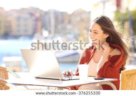Happy casual beautiful woman watching videos or enjoying entertainment content in a laptop sitting in a coffee shop terrace outdoors in a sunny day
