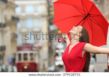 Portrait of a happy woman wearing red blouse under an umbrella breathing in the street of and old town in a rainy day