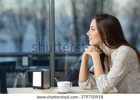 Profile portrait of a serious woman thinking in a coffee shop looking through the window in a bad day