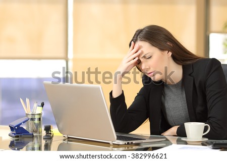 Businesswoman suffering migraines at job working on line with a laptop sitting in a desktop at office
