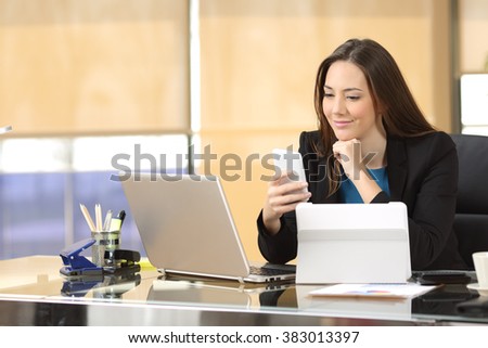 Relaxed businesswoman working with multiple devices holding a smartphone sitting in a desktop at office