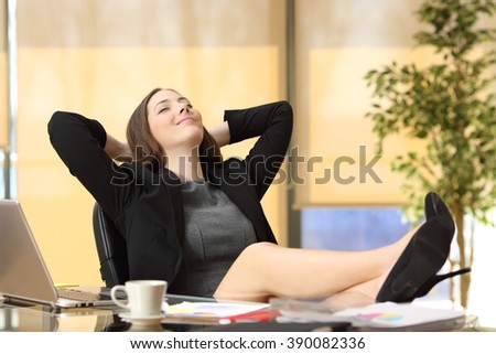 Satisfied relaxed businesswoman sitting in a chair with legs over the table and hands in the head enjoying her new job at office