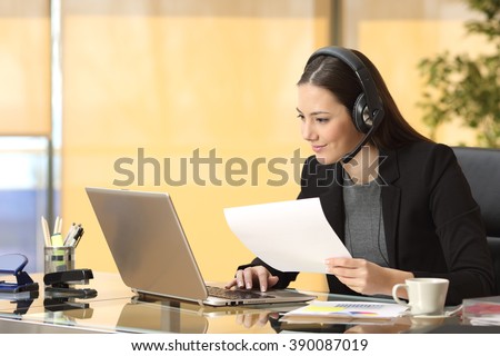 Freelance operator working online with a laptop and headsets and holding a document at office
