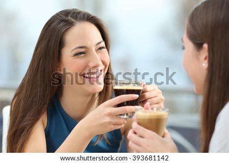 Portrait of two women friends talking holding coffee cups in a restaurant