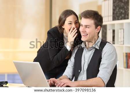 Gossip businesswoman telling secrets to the ear of a businessman sitting on a desktop at office