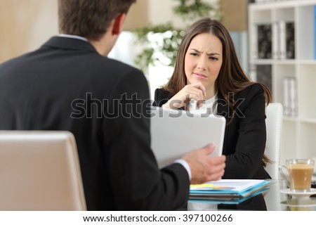 Salesman trying to convince a doubtful customer showing products in a tablet at workplace