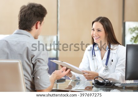 Happy doctor female wearing coat attending to her patient in a consultation while is holding a medical history sitting in a desktop