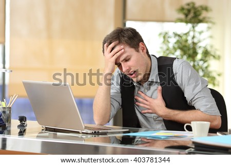 Businessman suffering an anxiety attack with the hands in his chest and head sitting in a desktop at office