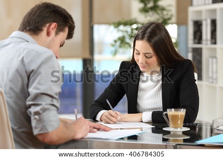 Two businesspeople signing contracts together after a deal in a desktop at office