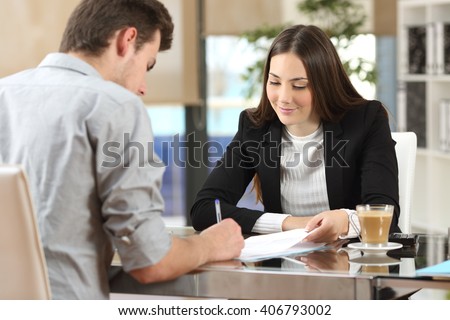 Client signing a document in an office with a businesswoman looking the contract