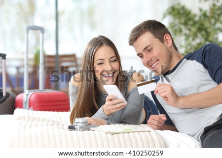 Couple of tourists ready for travel booking hotel on line with credit card and mobile phone on the bed