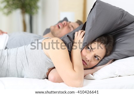 Man snoring while his wife is covering ears with the pillow