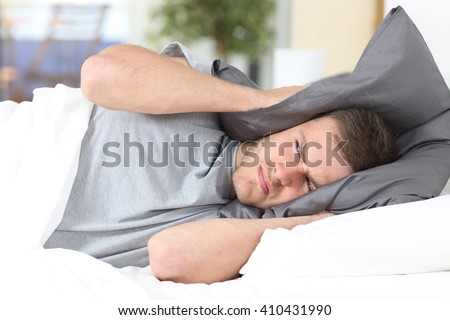 One man trying to sleep covering ears to avoid neighbor noise at home or hotel