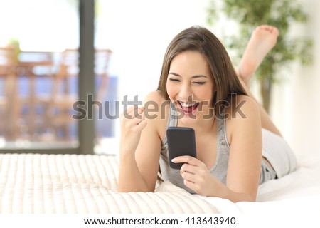 Excited winner checking online the phone for a prize lying on the bed at home with a window in the background