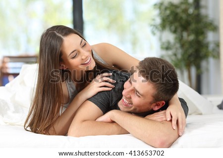Portrait of a happy couple or marriage having fun and joking looking each other on the bed of an hotel room or home