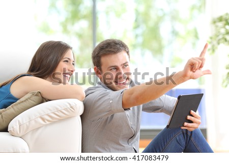 Happy couple sitting and planning new decoration with a tablet on line at home with a window in the background