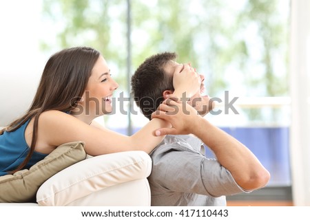 Playful couple covering eyes at home with a window in the background