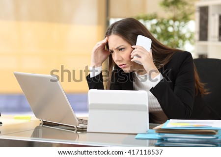 Worried executive talking on the phone trying to solve problems with multiple devices sitting in a desktop at office