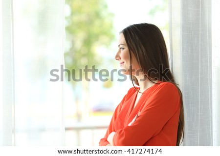 Side view portrait of a thoughtful attractive female looking the green background outside through a window of an hotel room or home