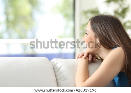 Portrait of a happy girl on a couch looking outdoors through a window