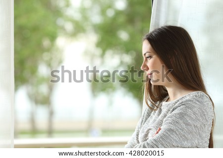 Profile portrait of a longing woman looking outdoors through a window at home or hotel room with a green background
