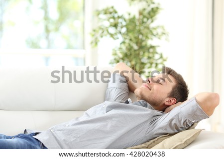 Relaxed man resting lying on a couch with the hands on the head at home