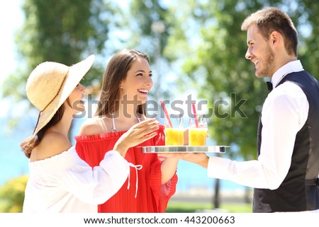 Two hotel customers on summer vacations and a waiter serving them drinks with the ocean in the background