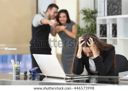 Two businesspeople bullying a sad colleague that is sitting in her workplace at office
