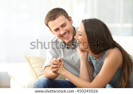 Happy couple or marriage looking each other laughing and holding hands sitting on a sofa at home