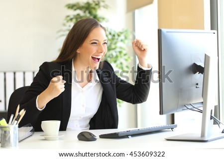 Excited executive wearing suit raising arms watching a desktop computer monitor at office