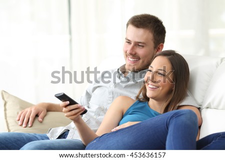 Happy couple watching tv at home sitting in a comfortable couch in the livingroom at home