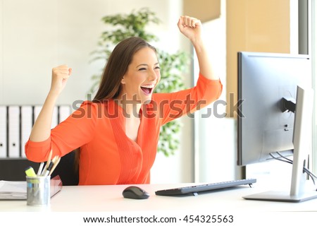 Excited entrepreneur wearing an orange blouse reading good news on line in a desktop computer monitor in the office