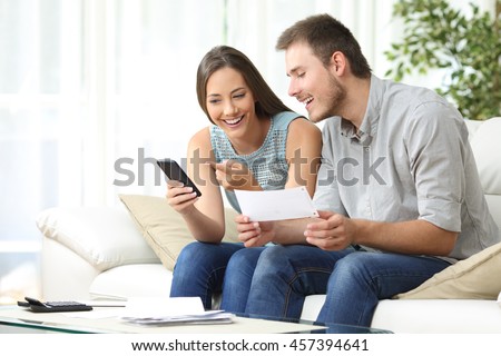 Couple doing accounting on line with a phone bank app sitting on a couch in the living room at home
