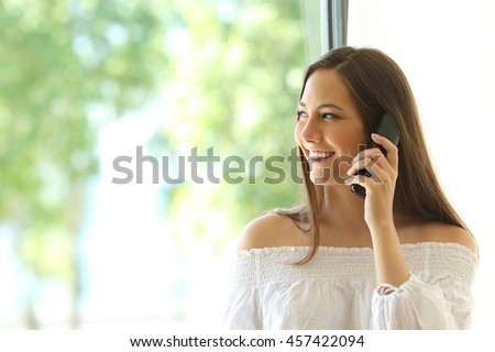 Girl calling on phone land line and looking outdoors through a window in the living room at home