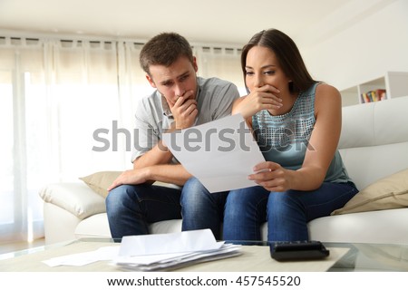 Worried couple reading a letter sitting on a couch in the living room at home