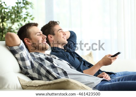 Side view portrait of two roommates watching tv sitting in a comfortable sofa in the living room at home