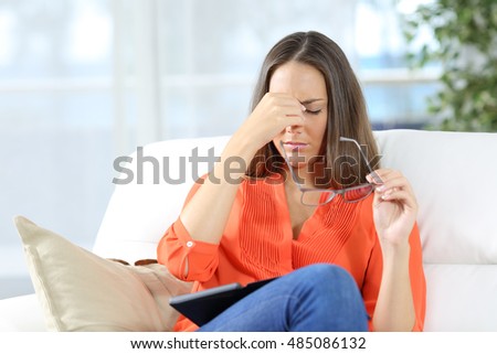 Woman with glasses suffering eyestrain after reading an ebook sitting on a couch at home