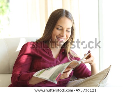 Happy woman reading a magazine sitting on a sofa in the living room at home