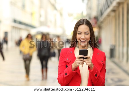 Front view of a fashion woman wearing red coat using a smart phone in winter and walking towards camera