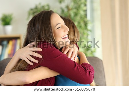 Two affectionate friends or sisters embracing with love in the living room at home