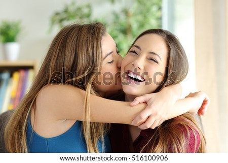 Affectionate girl kissing her happy sister or friend in the living room at home with a homey background