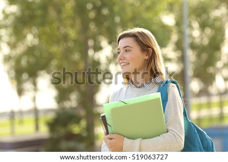 Happy beautiful student girl holding folders and books walking outdoors at sunset