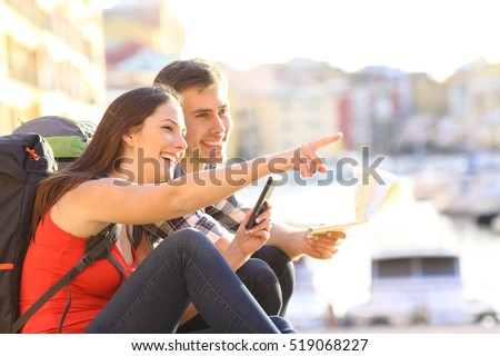 Side view of two happy tourists searching location together with a phone and map and pointing with the finger
