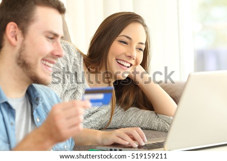 Close up of a happy couple buying on line with a credit card and a laptop on a couch in the living room at home
