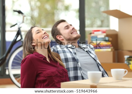 Happy couple sitting on the floor of the living room relaxing together while moving house with a window in the background