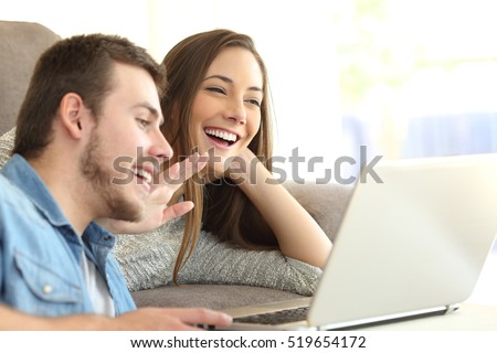 Happy couple talking and waving hand in a video conference on line with a laptop on a sofa at home