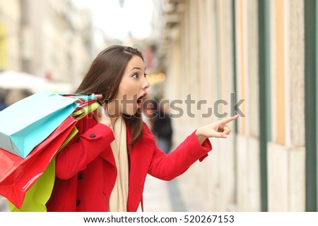 Amazed shopper opening mouth holding shopping bags watching special offers in stores and pointing in the street in winter